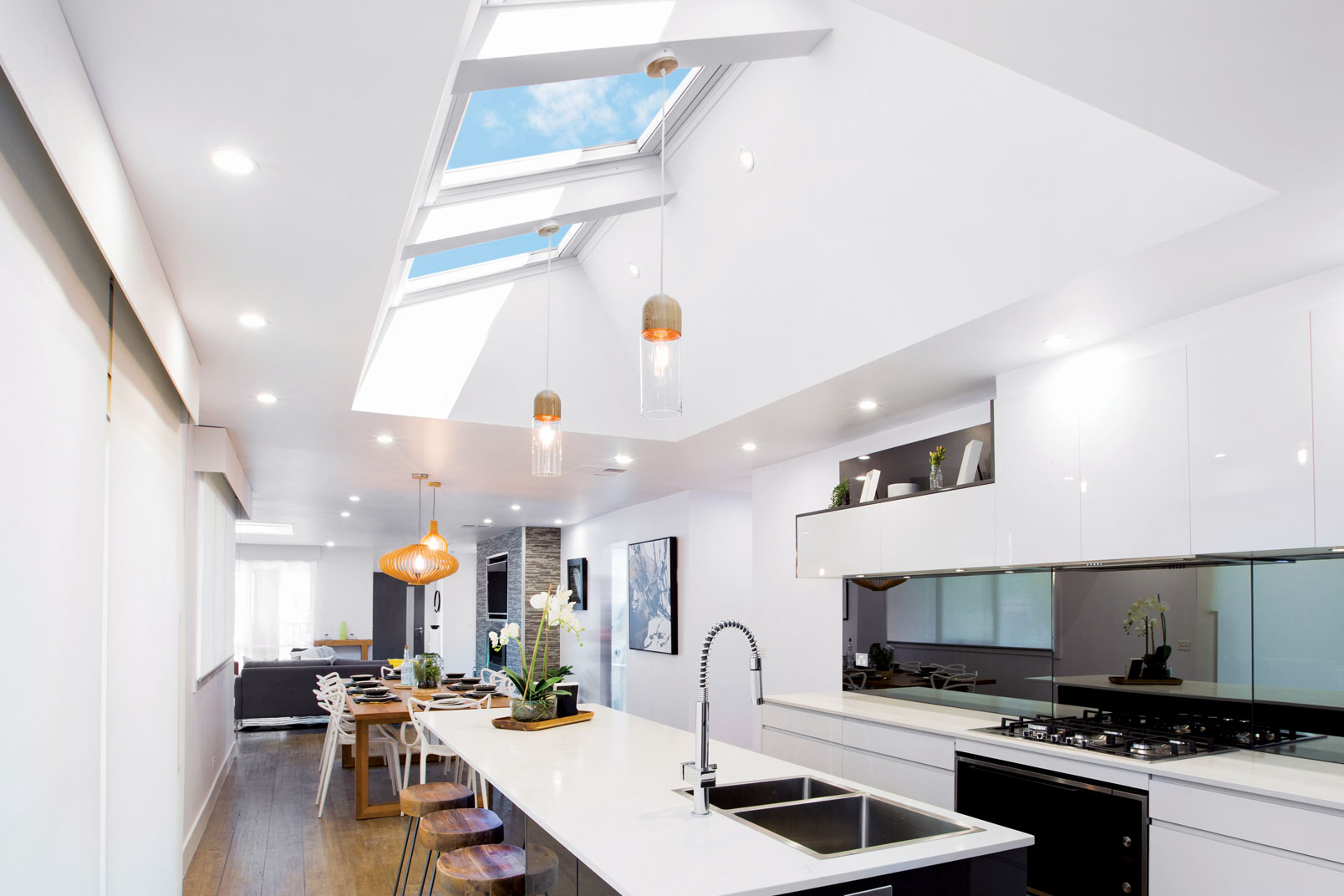 Bright white kitchen with skylights, a long island, pendant lights, and an open-plan dining area under a vaulted ceiling.