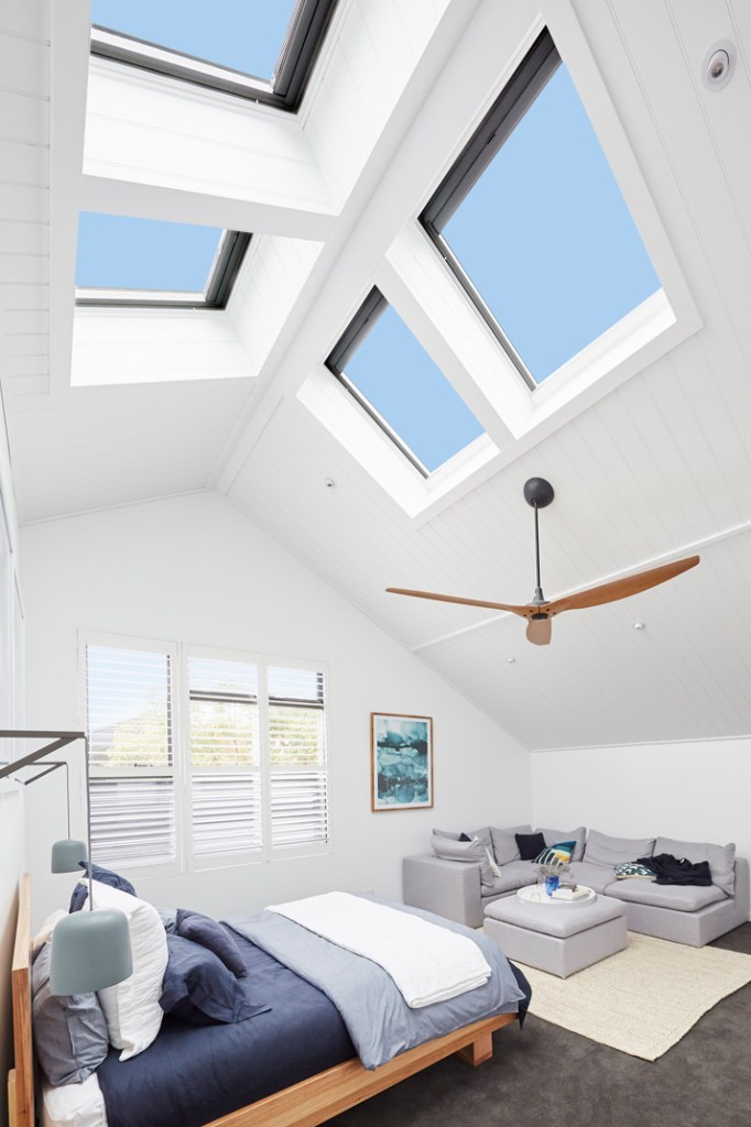 Bright bedroom with a pitched white ceiling, four skylights, ceiling fan, bed, shutters, sofa, and seating area