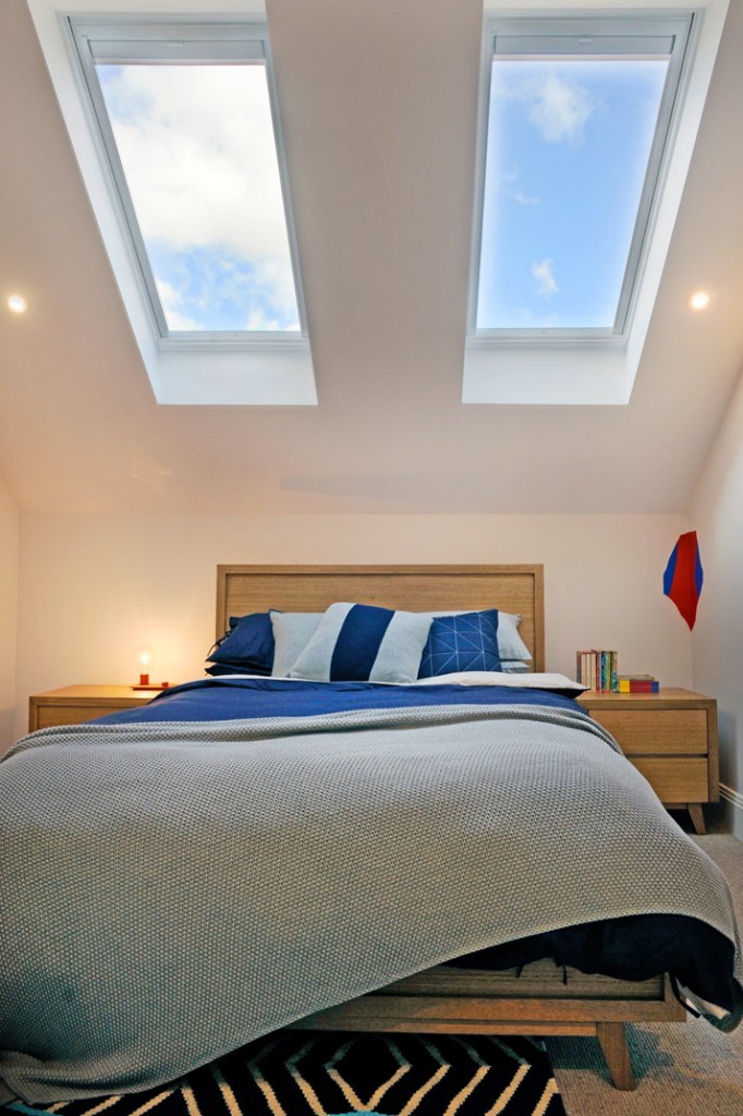 A neatly styled bedroom with two skylights, blue and white bedding, bedside tables, and a soft textured blanket.