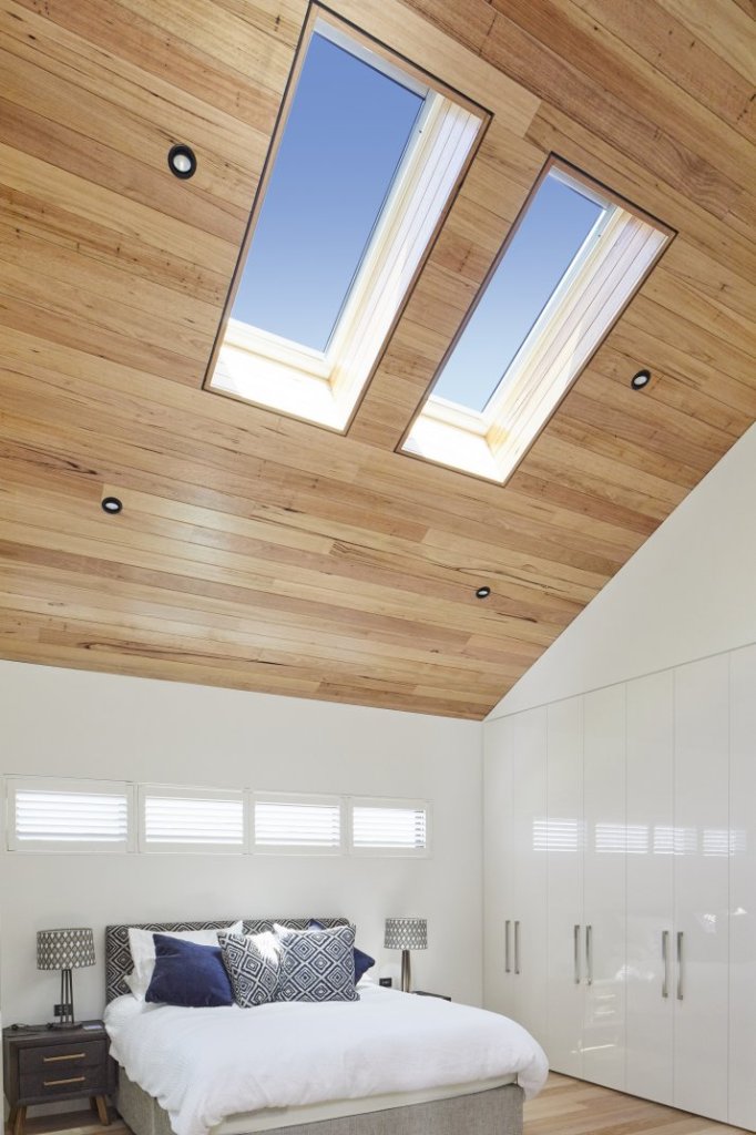 Bright bedroom with two skylights in a timber-lined ceiling, white wardrobes, plantation shutters, and a neatly made bed
