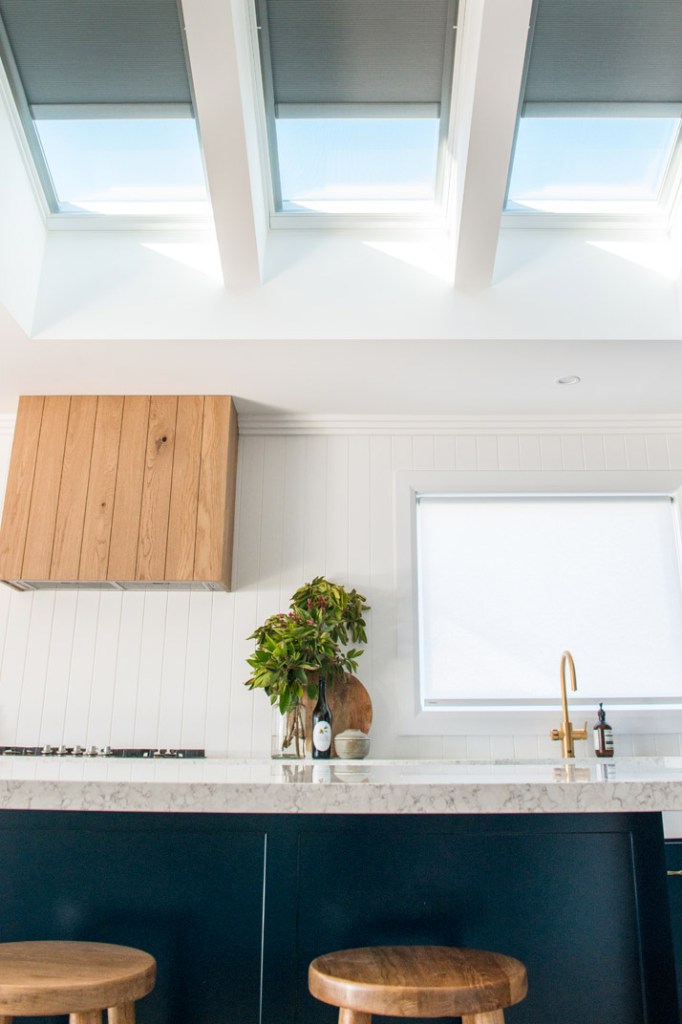 Bright kitchen with three roof skylights, a timber cabinet, indoor plant, marble counter, and gold faucet beneath a window