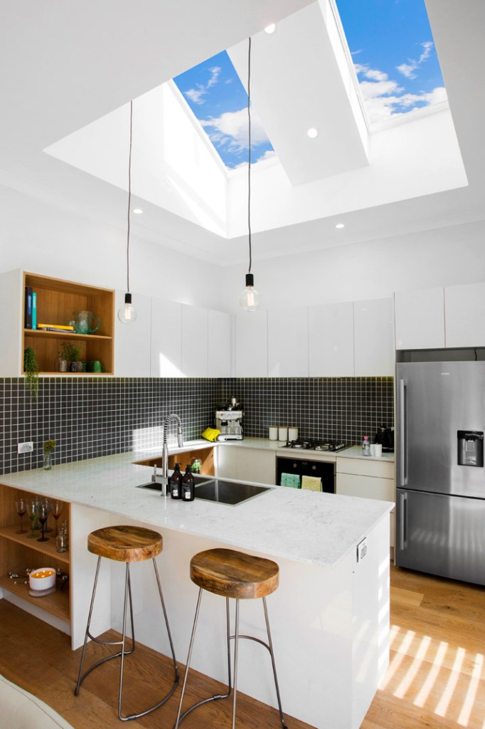 Bright white kitchen with skylights, pendant lights, marble island, timber stools, mosaic backsplash and steel refrigerator
