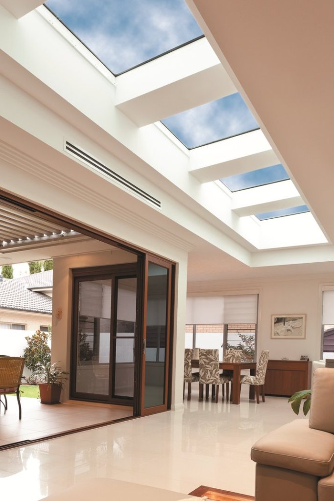 Bright open-plan living area with three large skylights, glass doors, polished floors, dining space, and a comfortable sofa.
