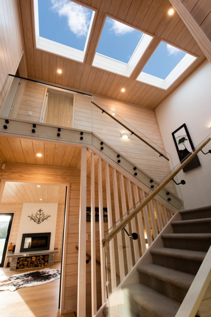A bright timber staircase rises beneath three skylights, with warm wood walls, recessed lights, and a nearby fireplace.
