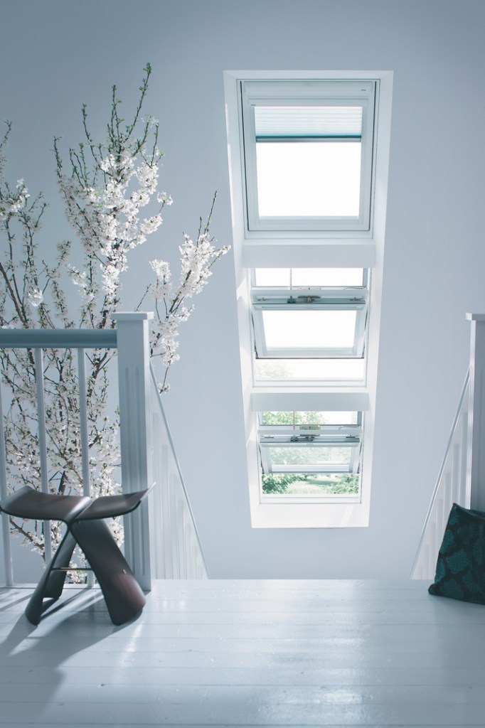 A bright attic stairwell with five aligned skylights, white walls, and blossoming branches visible beyond the glass.